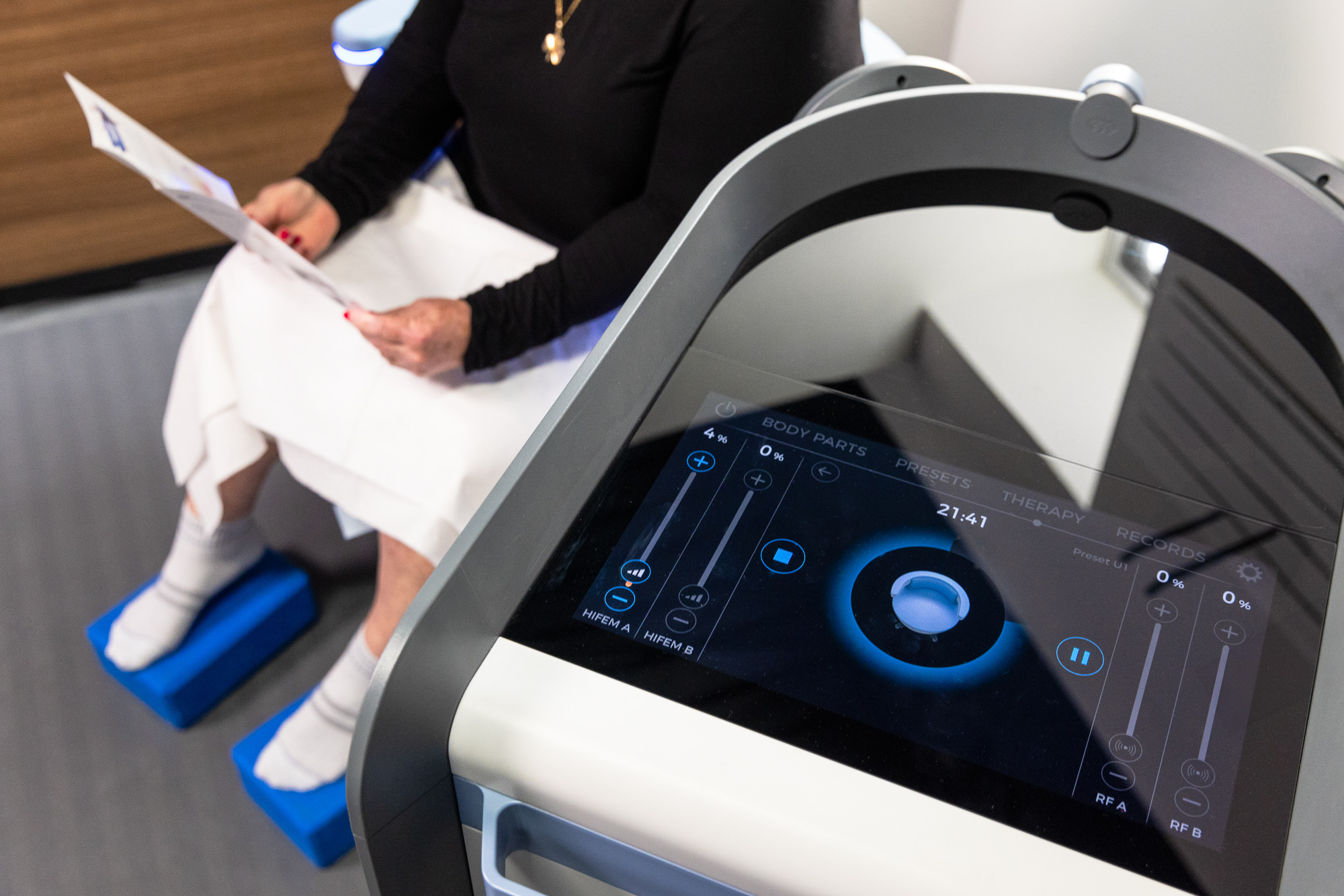 Close up of the digital control screen for Emsculpt Neo Near Arlington with a patient, sitting on Emsella in the background.