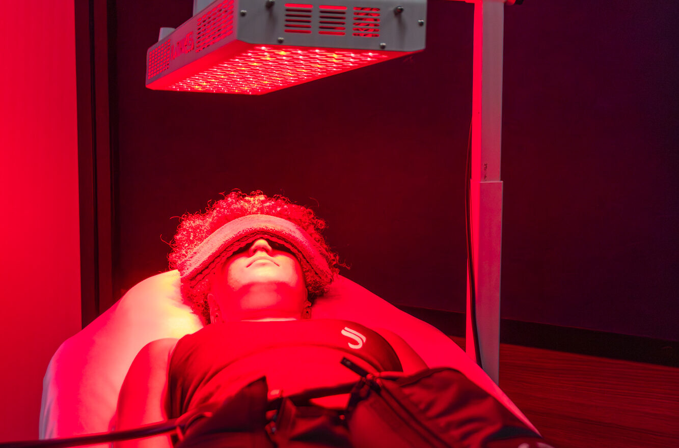 A female patient lying in a red light therapy bed with a folded towel covering her eyes. She is undergoing a skin toning treatment in Alexandria, VA.