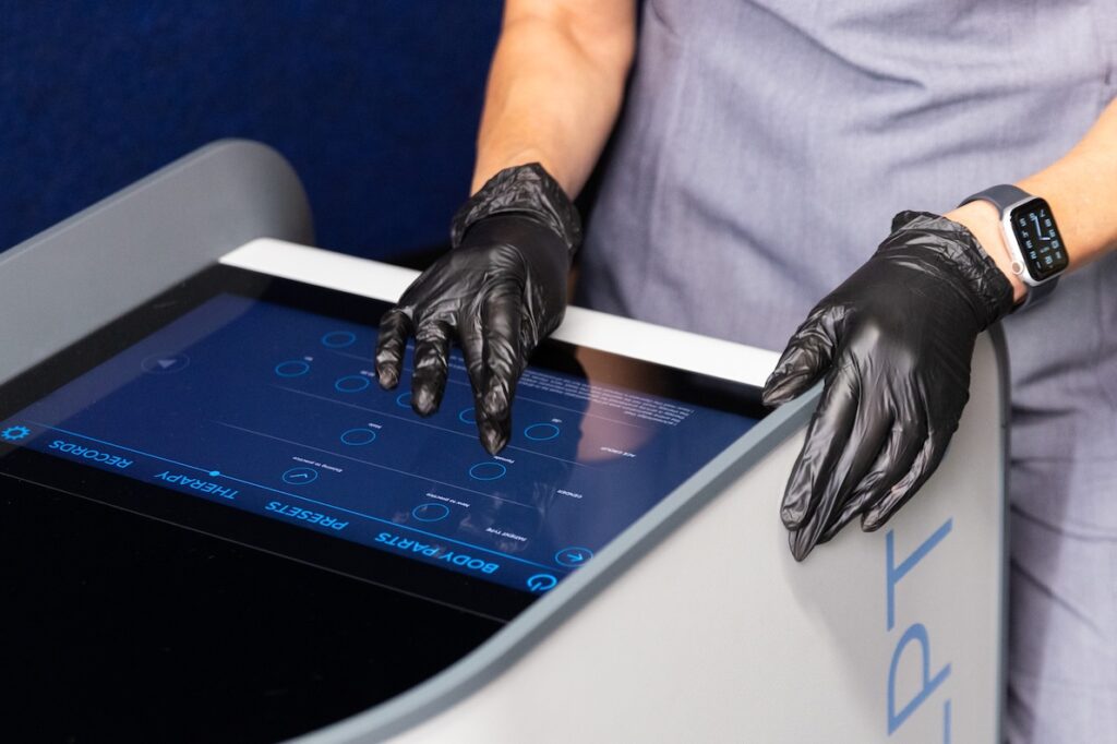 A provider adjusts the settings on the top of the workstation while treating a client with Emsculpt NEO near Fairfax, VA.